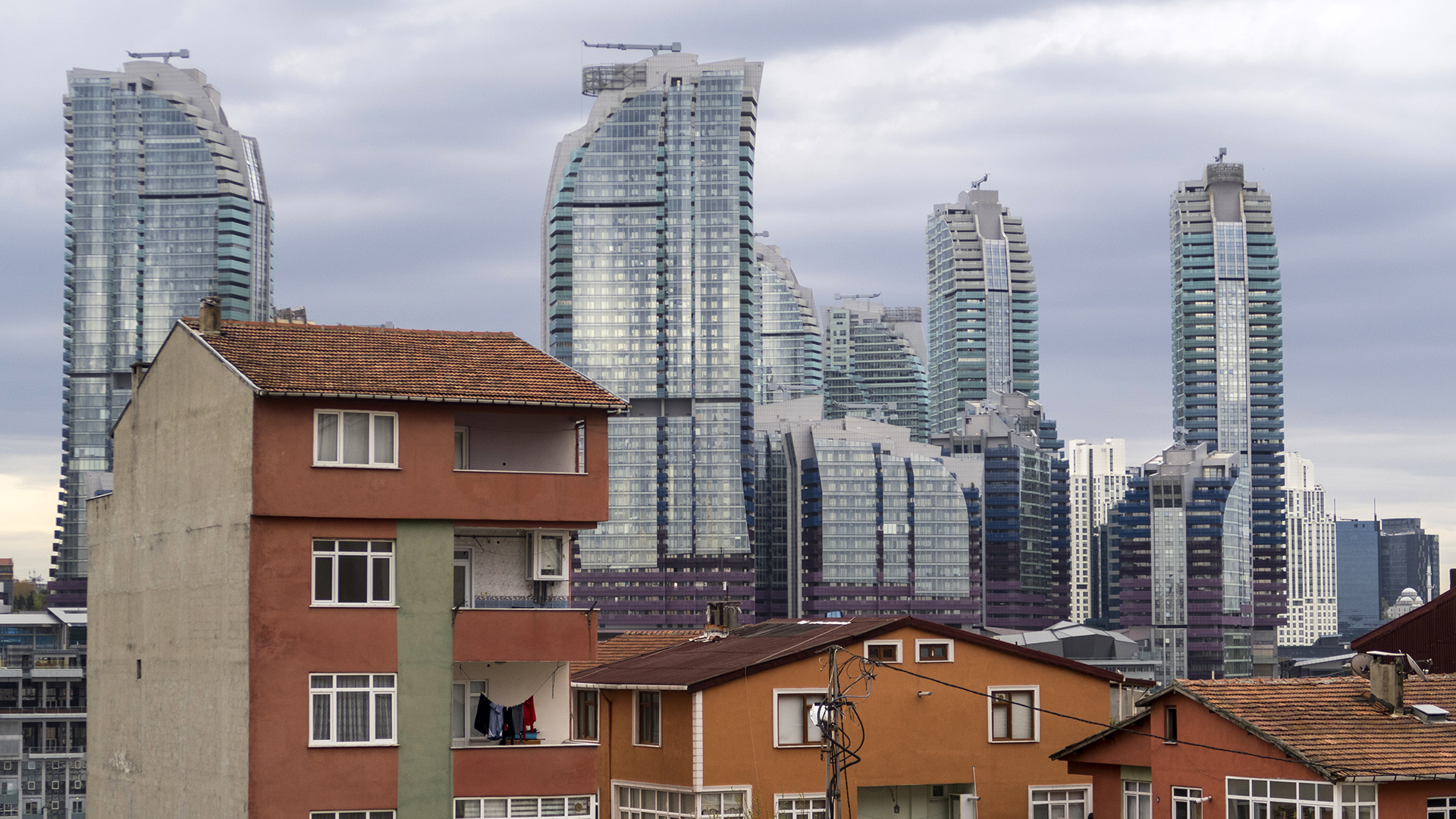 Turuncu renkli eski apartmanların arkasından gökdelen rezidansların yükseldiği bir manzara..