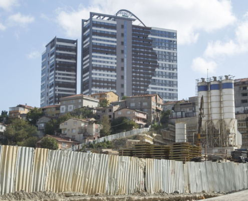 İstanbul Fikirtepe'den bir fotoğraf. Ön tarafta inşaat çitleri, çitlerin arkasında inşaat, az katlı konutlar ve onların arkasında yüksek katlı iki adet rezidans binası görünüyor.