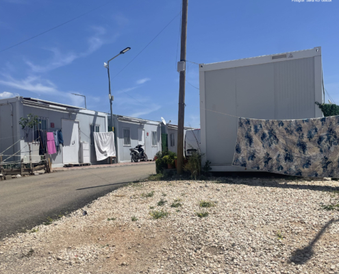 adiyaman2 Konteyner evlerin sıralandığı bir yerleşim alanı; çamaşırların asılı olduğu ipler, motosiklet ve saksılarla birlikte güneşli bir havada günlük yaşam düzeni görülüyor.